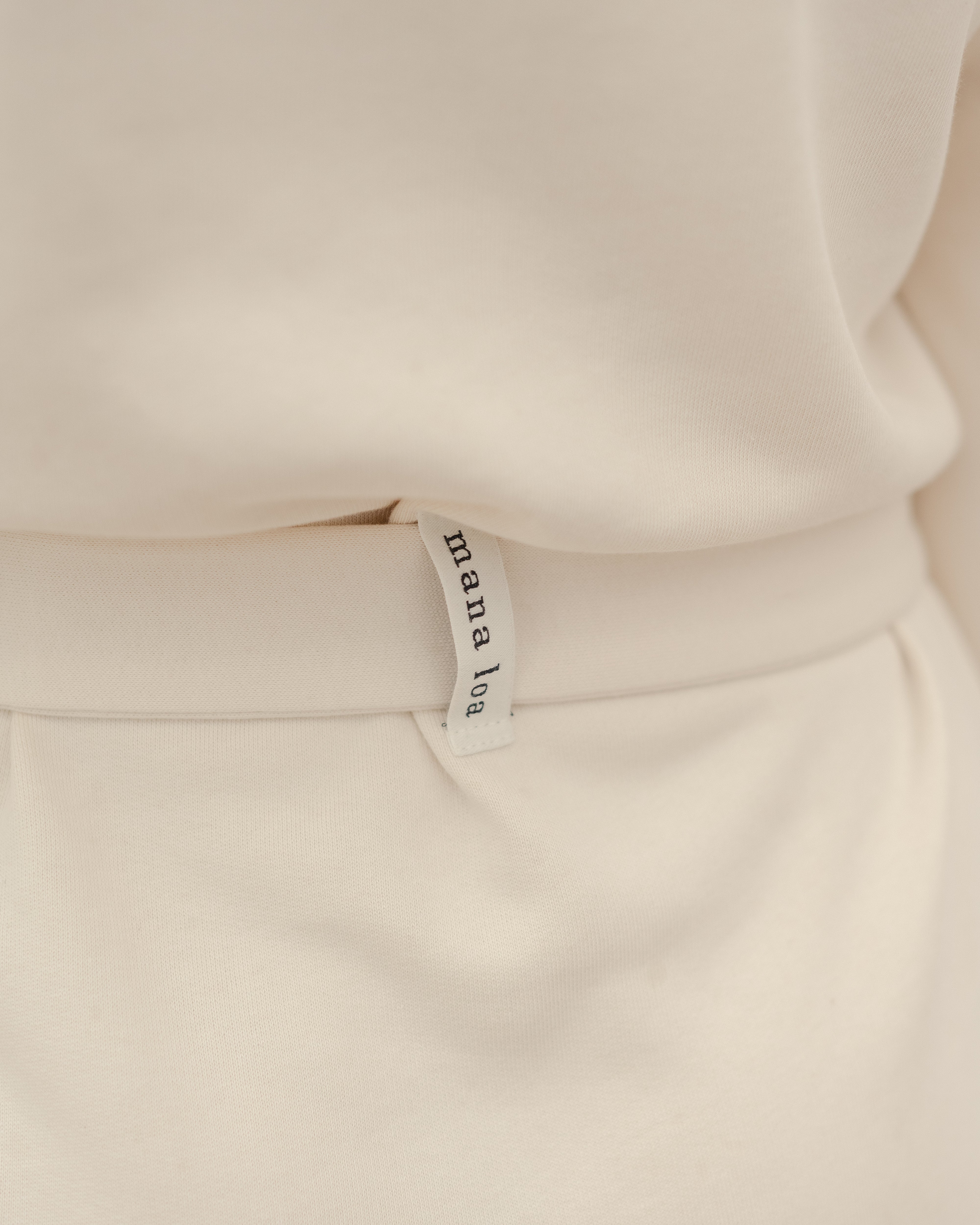 Detail of the back of a sweatshirt dress in ecru with belt and mana loa label, made of organic cotton.