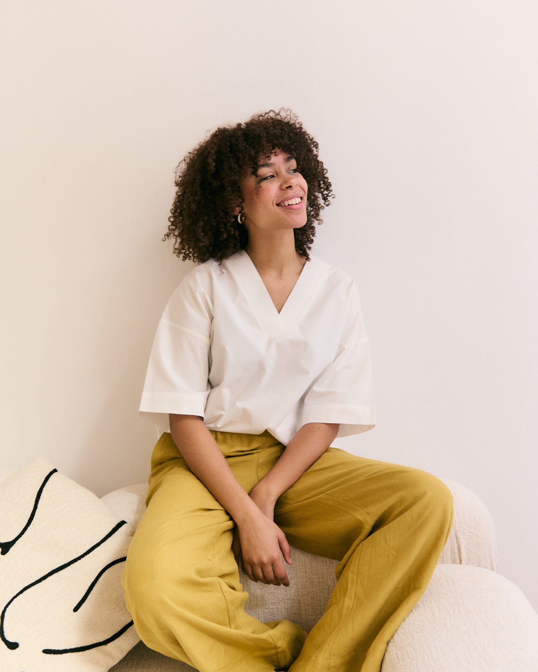 Woman in white oversized mana loa blouse made of 100% organic cotton and mustard-coloured linen trousers.