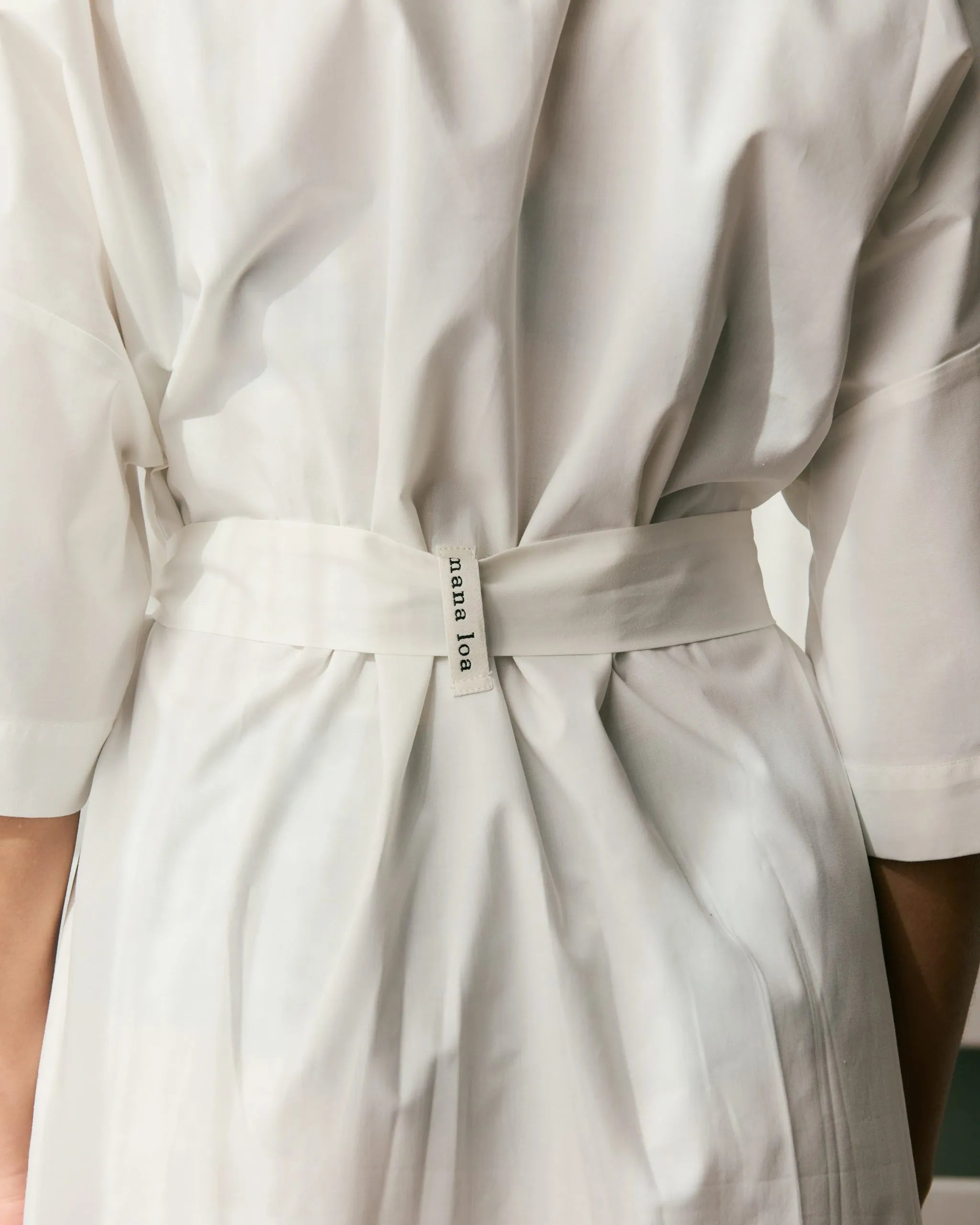 Detail of the back of an off-white organic cotton dress with a belt and the mana loa label.